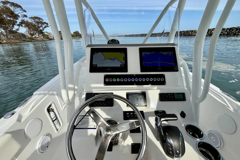 Slide: The Image of Edgewater 245CC 2023 boat dashboard with navigation screens and steering wheel on calm water. - 16