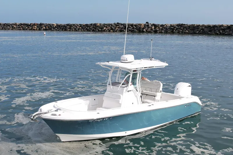 Slide: The Image of 2023 Edgewater 245CC boat on calm water near a rocky shoreline. - 2