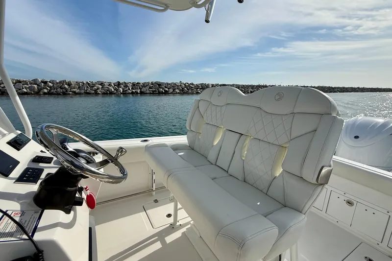 Slide: The Image of 2023 Edgewater 245CC boat interior with luxurious seating and steering wheel, docked by rocky shoreline. - 24