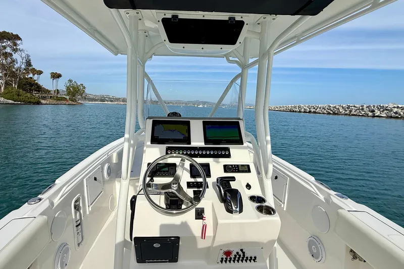 Slide: The Image of 2023 Edgewater 245CC boat dashboard with steering wheel and navigation screens on calm water. - 25