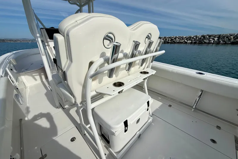 Slide: The Image of 2023 Edgewater 245CC boat interior with seating and rod holders, docked by rocky shoreline. - 26