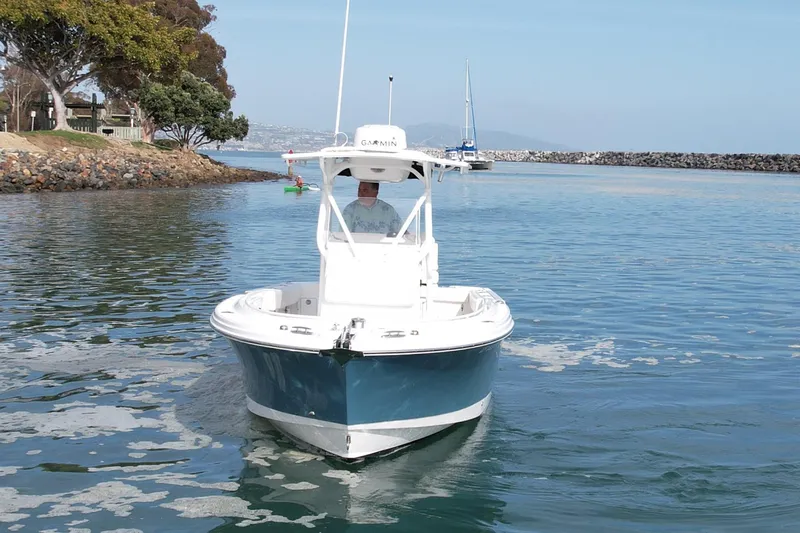 Slide: The Image of 2023 Edgewater 245CC boat navigating calm waters near a rocky shoreline. - 3