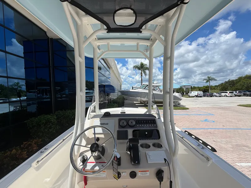 Slide: The Image of The image shows the cockpit of a 2027 Boston Whaler 210 Montauk. It features a modern helm with a steering wheel, instruments, and cup holders. A building and palm trees are visible in the background. - 14
