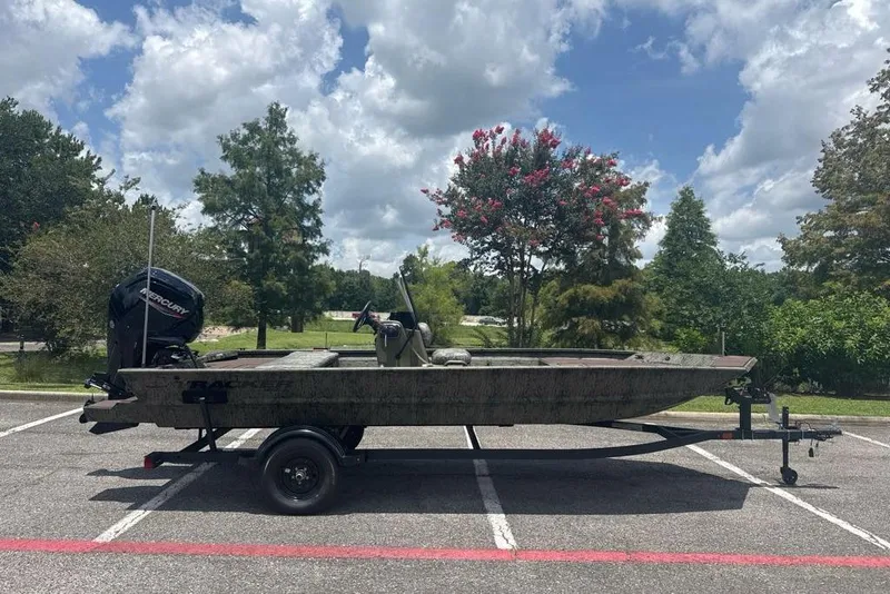 The Image of 2026 Tracker Grizzly 1860 CC boat on trailer in parking lot, surrounded by trees. - 0