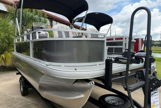 Slide: The Image of 2026 Sun Tracker Bass Buggy 16 XL Select pontoon boat on trailer, parked outdoors. - 2