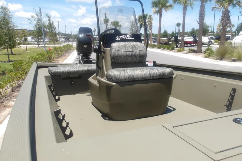 Slide: The Image of 2026 Tracker Grizzly 1860 CC boat with camouflage seating, parked outdoors under sunny skies. - 8