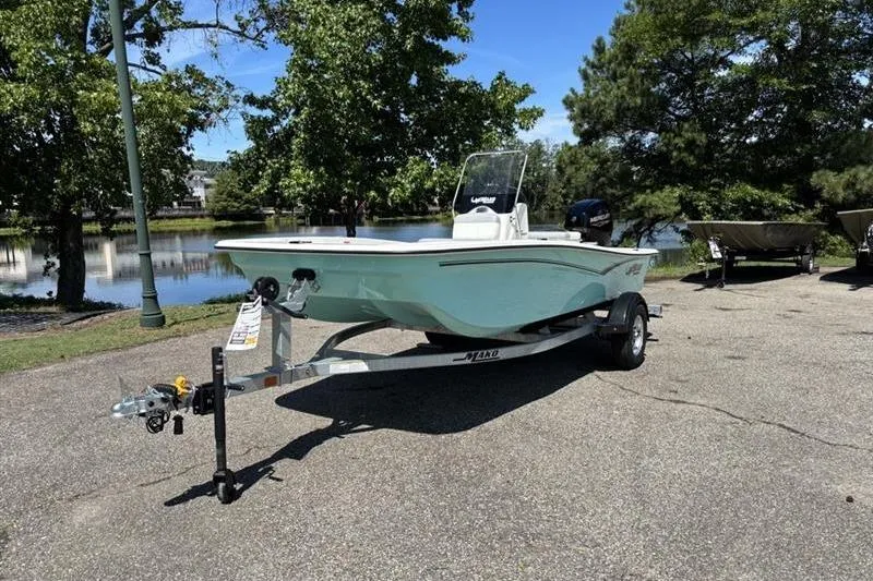 Slide: The Image of 2026 Mako Pro Skiff 15 CC boat on trailer, parked near a scenic lake. - 2