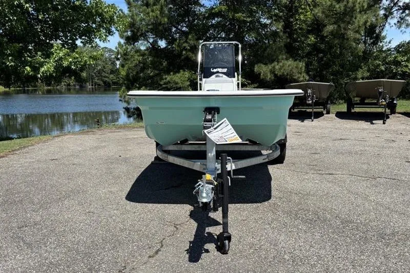 Slide: The Image of 2026 Mako Pro Skiff 15 CC boat on trailer by a lake, surrounded by trees. - 4