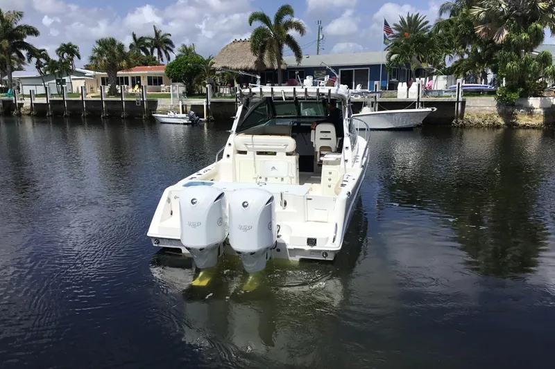 Slide: The Image of 2013 Everglades 320EX boat docked on a calm waterfront, surrounded by palm trees. - 10