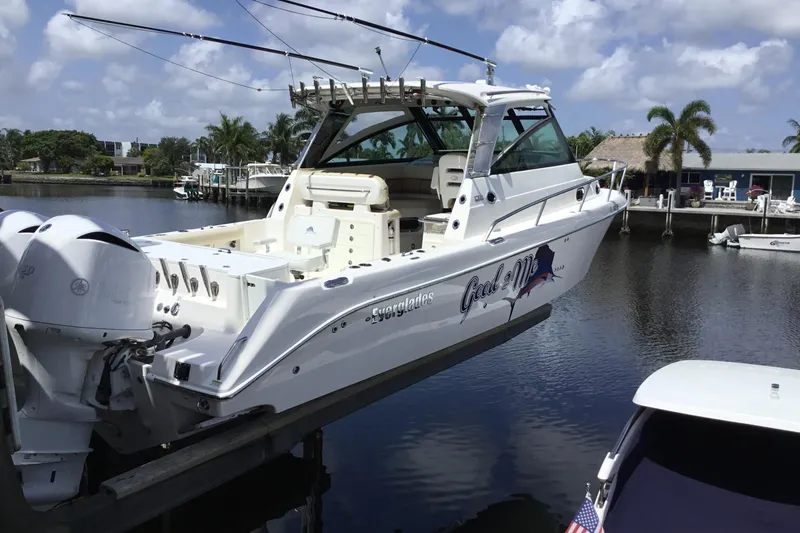 The Image of 2013 Everglades 320EX boat docked by a scenic waterfront with palm trees. - 0