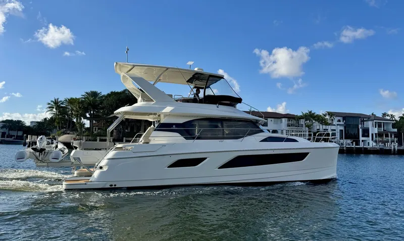Slide: The Image of 2022 Aquila 44 yacht cruising on a sunny day near waterfront homes. - 2