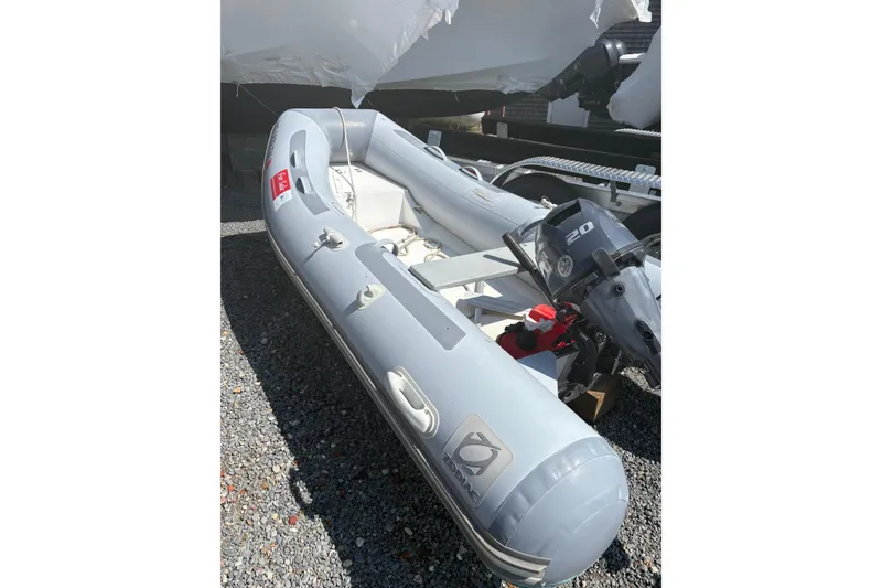 The Image of 2016 Zodiac Cadet RIB 340 PVC inflatable boat with outboard motor on gravel. - 0