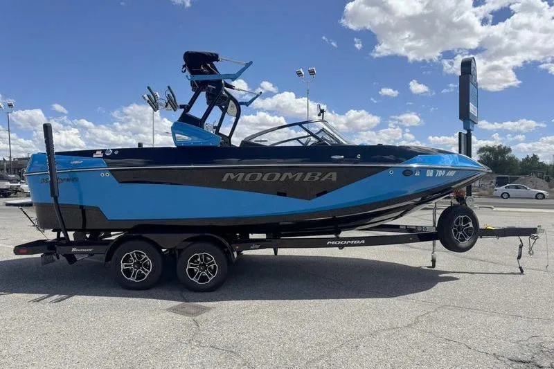 Slide: The Image of 2022 Moomba Kaiyen boat on trailer, blue and black design, parked outdoors. - 7