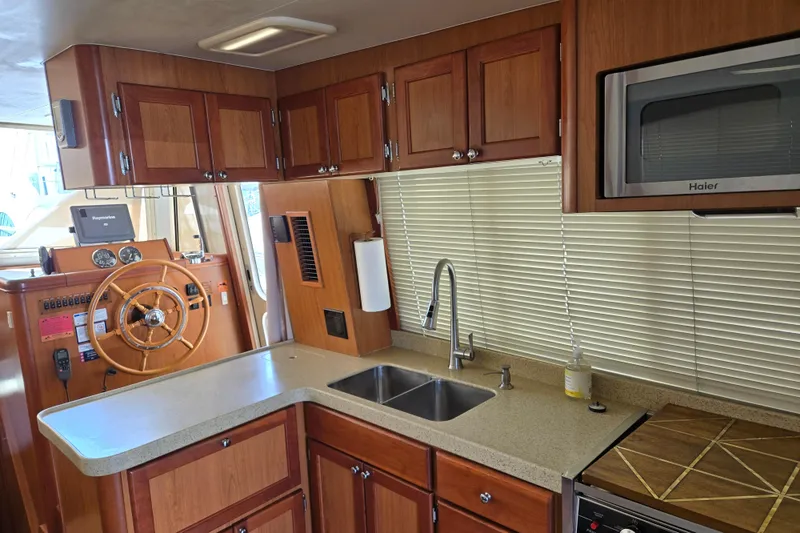 Slide: The Image of 2008 Mainship 400 Trawler kitchen with wooden cabinets, dual sink, and steering wheel. - 23