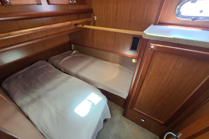 Slide: The Image of 2008 Mainship 400 Trawler cabin with twin beds, wooden cabinetry, and a small window. - 32