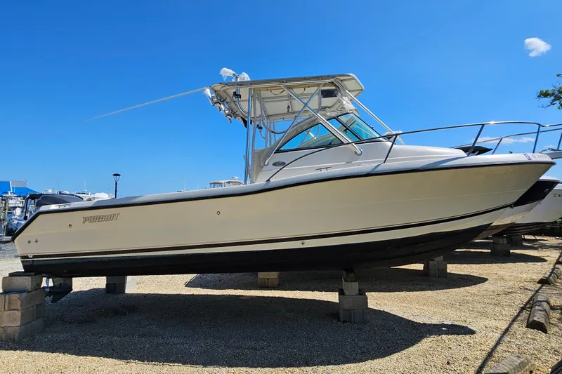 The Image of 2004 Pursuit 2470 Walkaround boat on blocks, displayed outdoors under clear blue sky. - 1