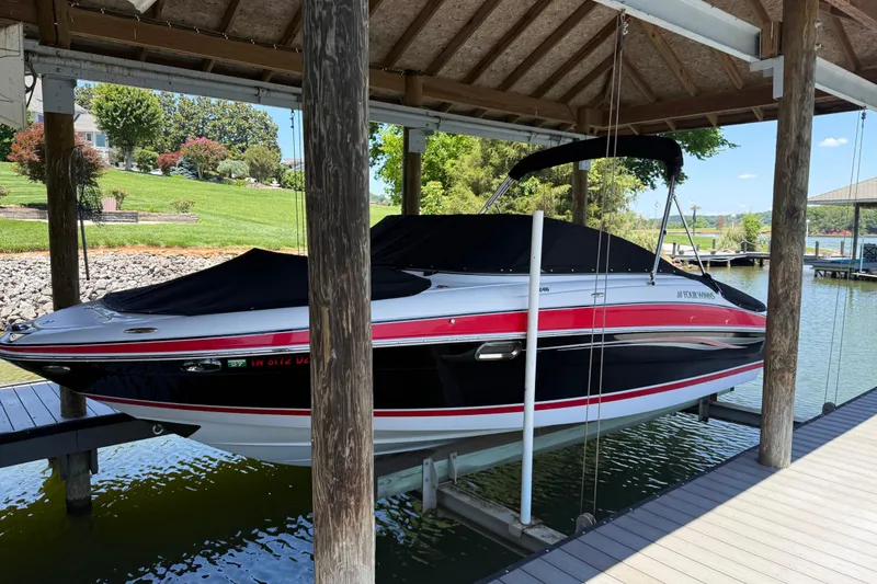 The Image of 2007 Four Winns H240 boat docked under a wooden canopy, covered and elevated above water. - 1