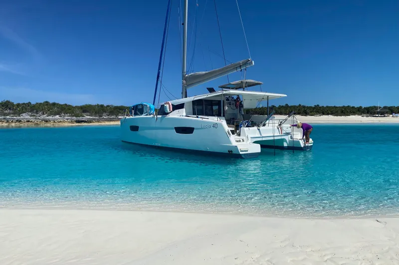 The Image of 2018 Fountaine Pajot Lucia 40 catamaran anchored in clear turquoise waters near a sandy beach. - 0