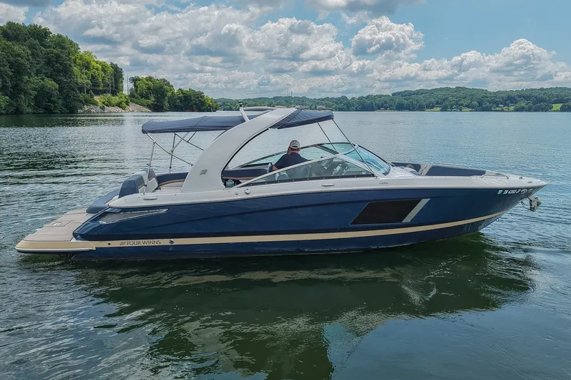 Slide: The Image of 2014 Four Winns H290 boat on a serene lake with lush green shoreline. - 1