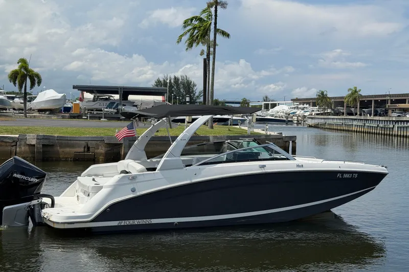 Slide: The Image of 2023 Four Winns HD5 OB boat docked in a marina with palm trees and cloudy sky. - 11