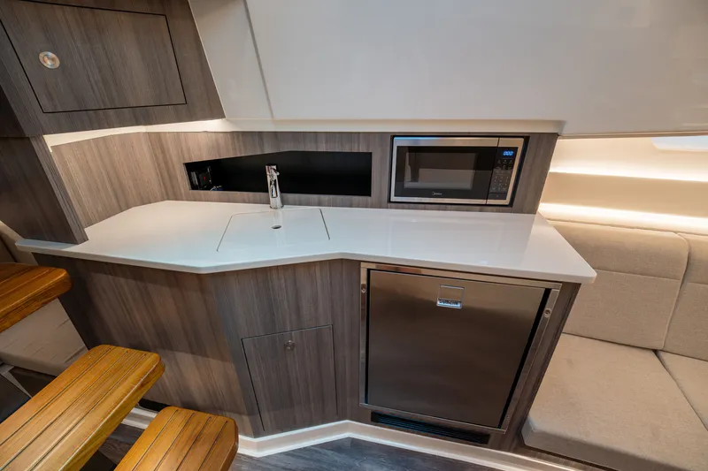 Slide: The Image of The cabin of the 2026 Sea Ray Sundancer 370 Outboard features a modern kitchenette with a microwave and fridge. - 38