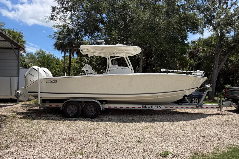 Slide: The Image of 2019 Jupiter 30 boat on Blue Fin trailer, parked outdoors with trees in the background. - 3