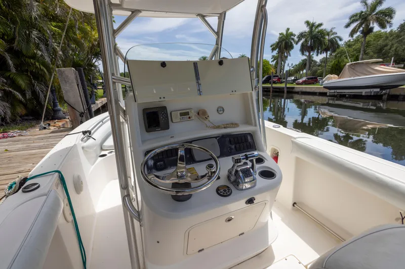 Slide: The Image of 2007 Boston Whaler 270 Outrage boat cockpit with steering wheel and controls, docked by palm trees. - 8