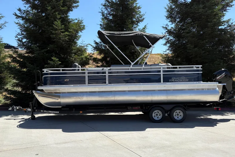 The Image of 2026 Sun Tracker Sportfish 24 XP3 pontoon boat on trailer, parked outdoors. - 0