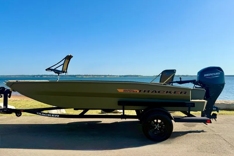 Slide: The Image of 2026 Tracker Grizzly 1756 T Marsh boat on trailer by a lake under clear blue sky. - 13