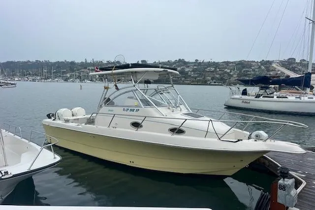 Slide: The Image of 1998 Pro-Line 2610 Walkaround boat docked in a marina with scenic background. - 2