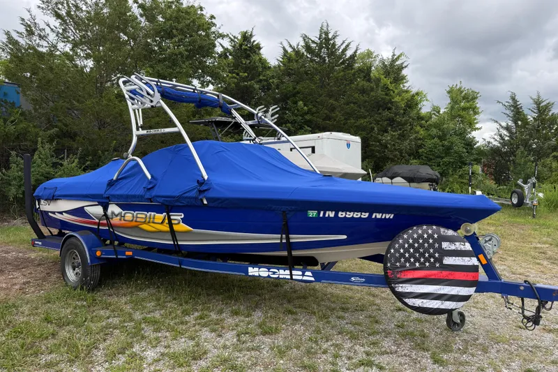 Slide: The Image of 2002 Moomba Mobius LSV boat with blue cover on trailer, parked outdoors. - 2