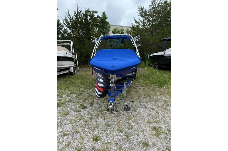 Slide: The Image of 2002 Moomba Mobius LSV boat with blue cover, parked on gravel near trees. - 9