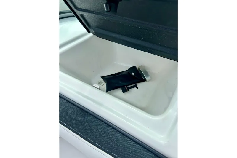 Slide: The Image of Open storage compartment in a 2015 Yamaha AR210 boat, featuring a black accessory inside. - 38
