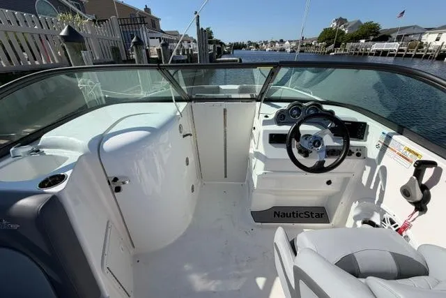 Slide: The Image of 2023 NauticStar 223 DC boat interior with steering wheel and dashboard, docked by waterfront homes. - 17