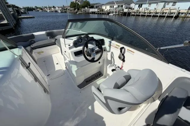 Slide: The Image of 2023 NauticStar 223 DC boat interior with steering wheel, seating, and dashboard by the water. - 18