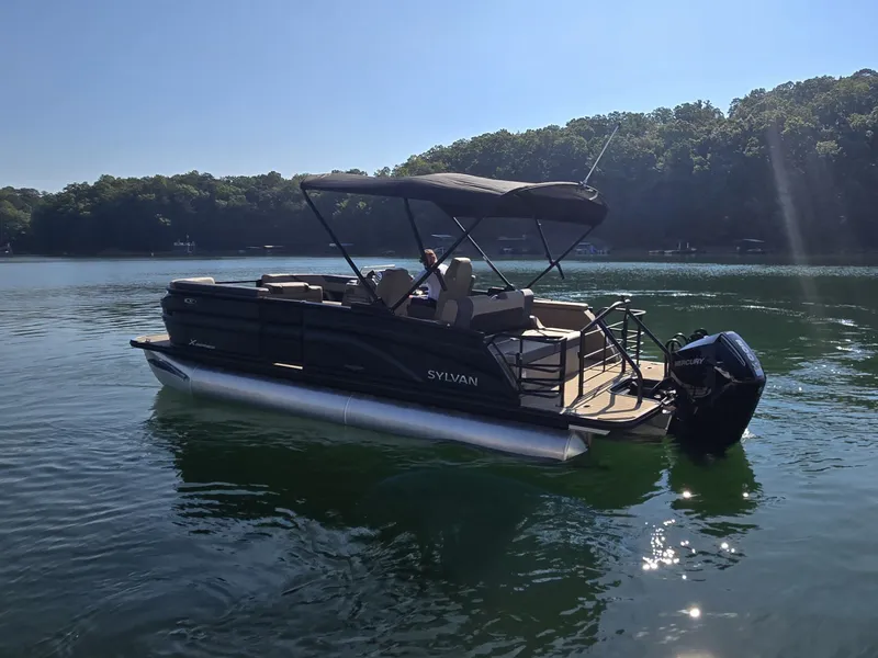 Slide: The Image of A 2027 Sylvan MIRAGE X3 ULZ pontoon boat on a calm lake with a wooded shoreline. - 28