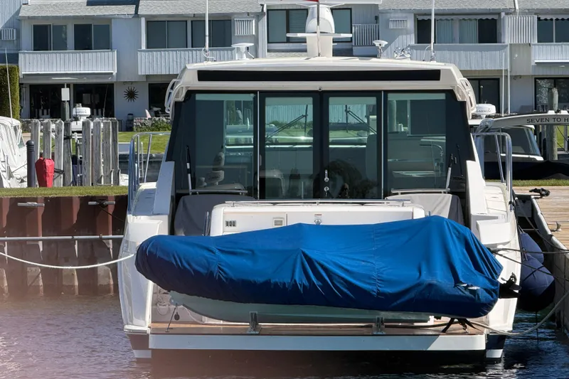 Slide: The Image of 2019 Tiara Yachts C44 Coupe docked, rear view with blue cover, waterfront background. - 4