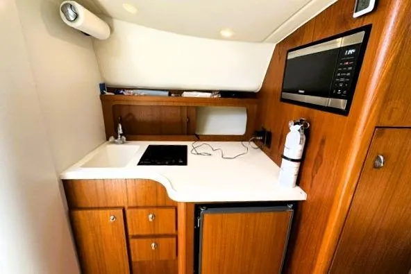 Slide: The Image of 2001 Tiara Yachts 2900 Open galley with sink, stove, microwave, and wooden cabinetry. - 14