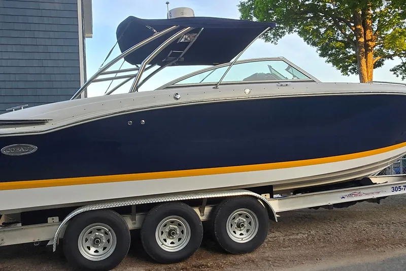 Slide: The Image of 2013 Cobalt 296 boat on trailer, navy blue with yellow stripe, parked outdoors. - 1