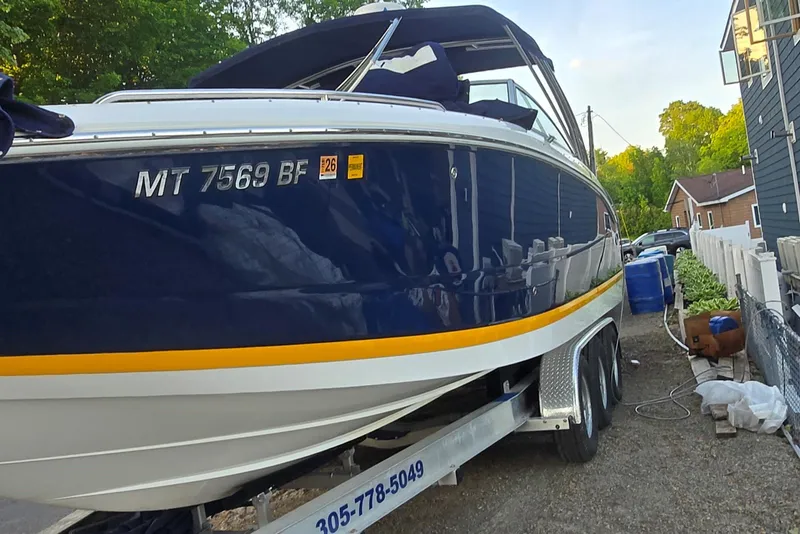 Slide: The Image of 2013 Cobalt 296 boat on trailer, blue and white with yellow stripe, parked outdoors. - 2