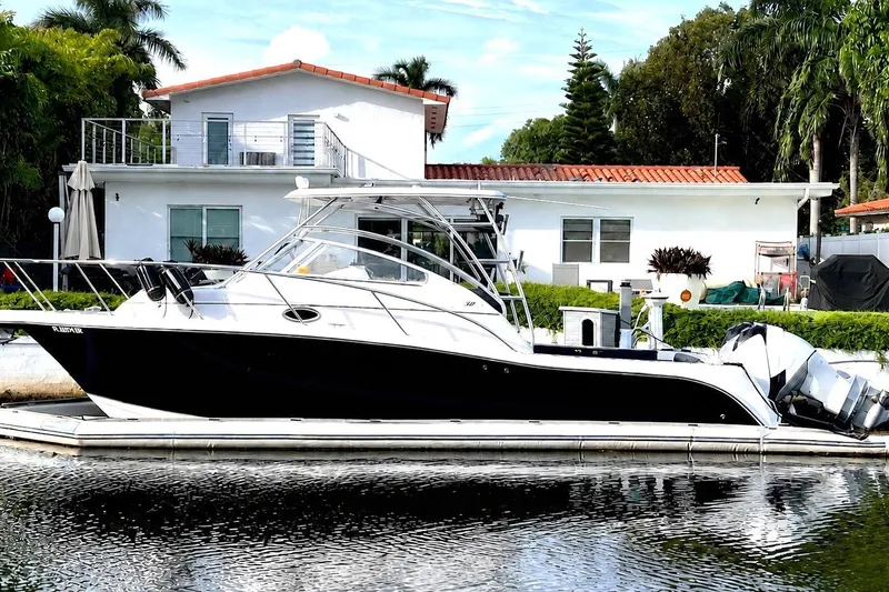 The Image of 2006 Pro-Line 32 Express boat docked by a waterfront house with lush greenery. - 0
