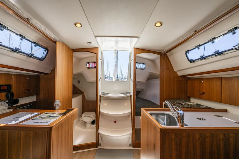 Slide: The Image of Interior of 2018 J Boats J/97E sailboat, featuring wood cabinetry, kitchenette, and compact bathroom. - 18