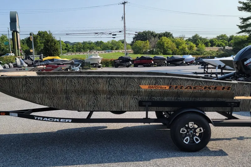 The Image of 2026 Tracker Grizzly 1756 T Marsh boat on trailer, camo design, parked outdoors. - 0