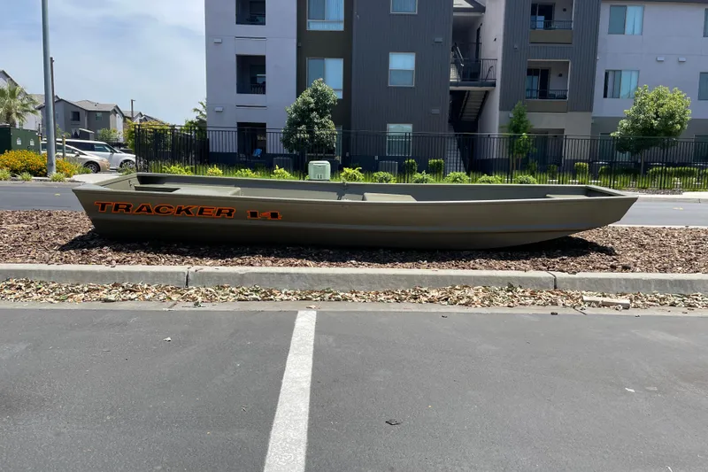 The Image of 2026 Tracker Grizzly 14 Jon boat parked on landscaped area near modern apartments. - 0