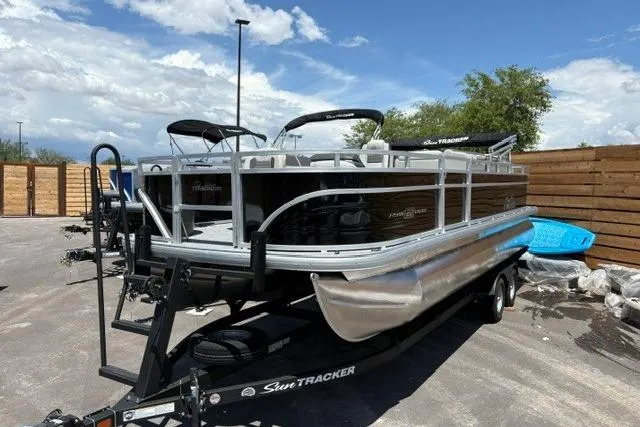 The Image of 2026 Sun Tracker Fishin' Barge 22 DLX pontoon boat on trailer, parked outdoors. - 0