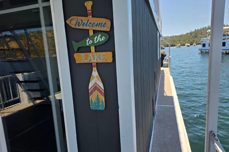 Slide: The Image of Houseboat with "Welcome to the Lake" sign, docked on a scenic lake, 2007 Custom model. - 5
