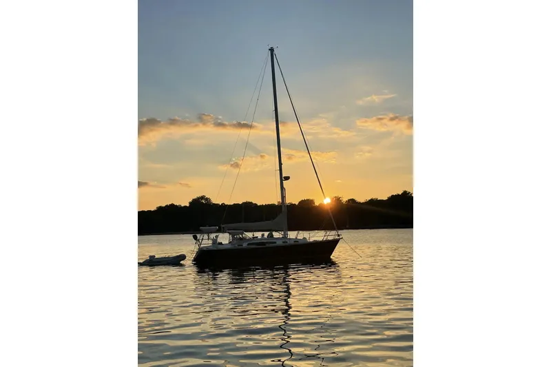 The Image of Sailboat Sabre 36 (1998) on tranquil water at sunset, silhouetted against a colorful sky. - 0