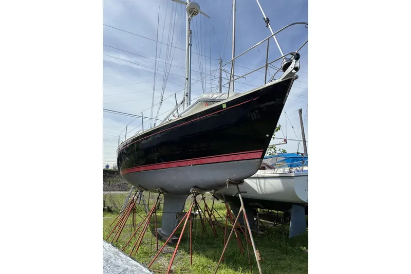 Slide: The Image of 1998 Sabre 36 sailboat on stands, black hull with red stripe, outdoor setting. - 2