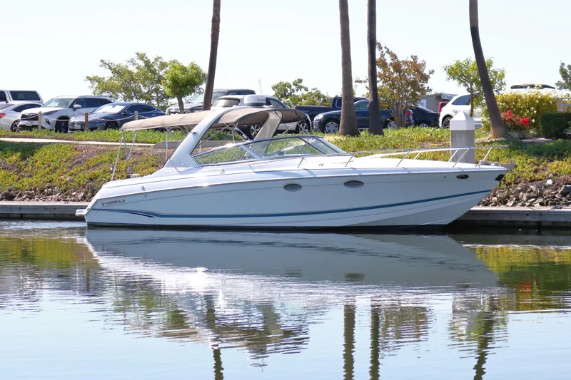 The Image of 2006 Formula 330 Sun Sport boat docked on calm water, surrounded by greenery and parked cars. - 1