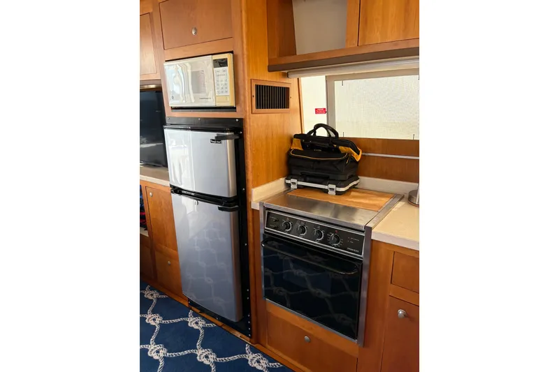 Slide: The Image of 2003 Mainship 390 Trawler kitchen with fridge, oven, and microwave in wooden cabinetry. - 19